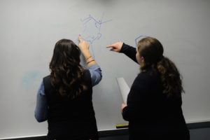 two students facing a white board working on an assignment
