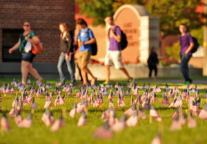 Lake State students walking through campus on a sunny day surrounded by small American flags placed in the ground to remember 9 -11