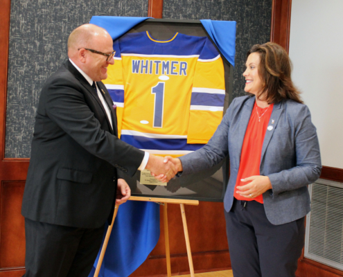 LSSU President Hanley and Governor Whitmer shake hands as she accepts a personalized jersey from LSSU