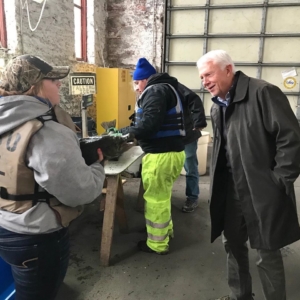 Representative Jack Bergman visits the CFRE Hatchery where student Dakota is showing him one of the salmon. In the background, students are measuring salmon.