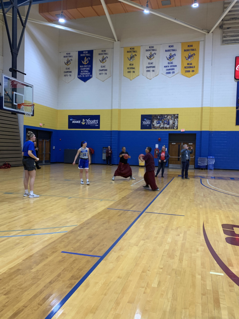 Monks shooting basketballs with women's Laker basketball team
