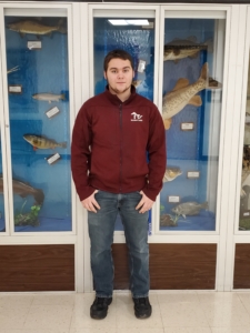 A male student is standing in front of a glass case of fish mounts