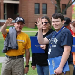Incoming student and family smile and wave at camera in line for lunch at orientation.