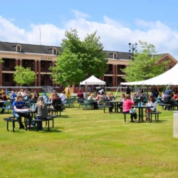Orientation attendees eat lunch at picnic tables on Pledger Commons with Brady Hall in the background.