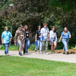 Small group of incoming students walk across campus with admissions representative.