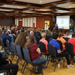 Seated crows of incoming students and families as University President Dr. David Travis speaks in front of the group.