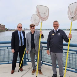Representatives from Cloverland Electrical Cooperative, LSSU, and the MI Department of Natural Resources hold nets as they stand near the rail.