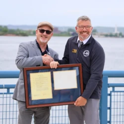 LSSU President Dr. David Travis presents proclamation document to MDNR representative. They shake hands as they each hold the frame.