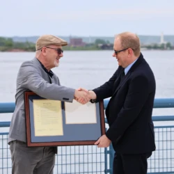 LSSU President Dr. David Travis presents proclamation document to Cloverland Electrical Cooperative representative. They shake hands as they each hold the frame.