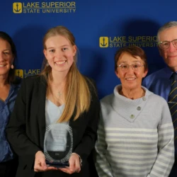 Outstanding undergraduate student recipient and her family in front of LSSU backdrop.