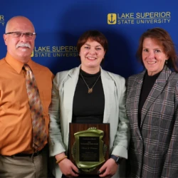 Outstanding young alumni award recipient and her family in front of LSSU backdrop.
