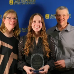 Outstanding regional center graduate award recipient and her family in front of LSSU backdrop.