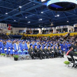 Full crowd of students, faculty, and attendees both seated on the floor and in the stands at the commencement ceremony.