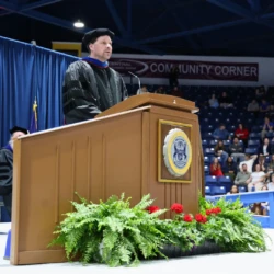 Faculty Speaker and award recipient at commencement podium addressing graduates.
