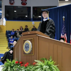 Invited speaker and honorary doctorate recipient at commencement podium addressing graduates.
