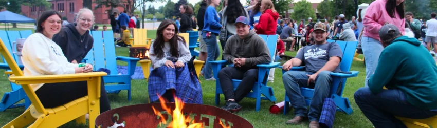 Students gathered around bonfire ring featuring 'Lakers' text, smiling and facing the camera for a posed shot at orientation.