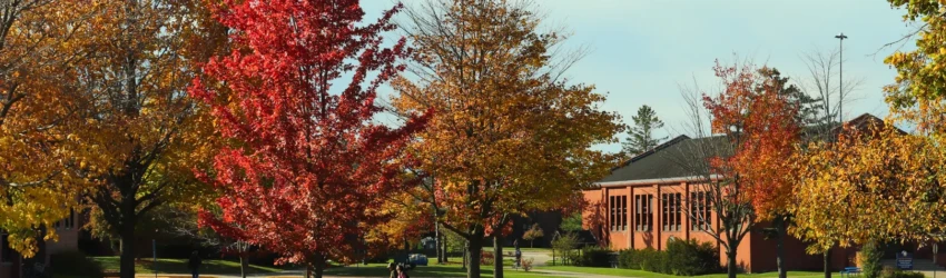 Two students are seen walking across campus with Fall colored trees in the foreground and the Fletcher Center in the background.