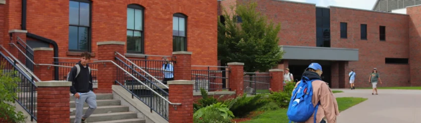 Students walking throughout campus with two academic building visible in the background.