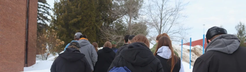 A group of students and their families tour LSSU in the winter, with a drawstring bag featuring LSSU's logo highlighted.