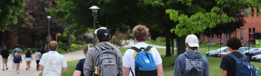 A tour group walks across campus, wearing backpacks as they look ahead towards the Center for Applied Sciences.