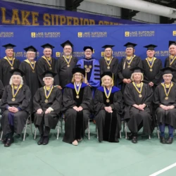 Golden grads with University President in front of LSSU backdrop prior to commencement ceremony.