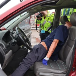 Decoy body in car being photographed by criminal justice student during simulation.