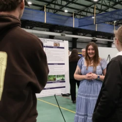 Graduating senior speaking with attendees about research.