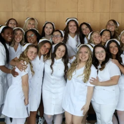 Full group of nursing pinning graduates in Arts Center lobby, dressed in white.