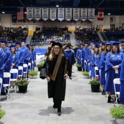 Last year's faculty speaker leads the line of faculty at commencement ceremony, carrying a ceremonial torch.
