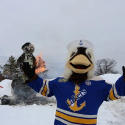 Seamore the Seaduck in Laker Hockey jersey in front of a burning paper mache snowman.
