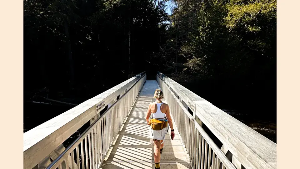 Person hiking across bridge crossing falls.