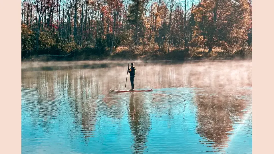 Paddleboarder on water in the foggy morning hours.